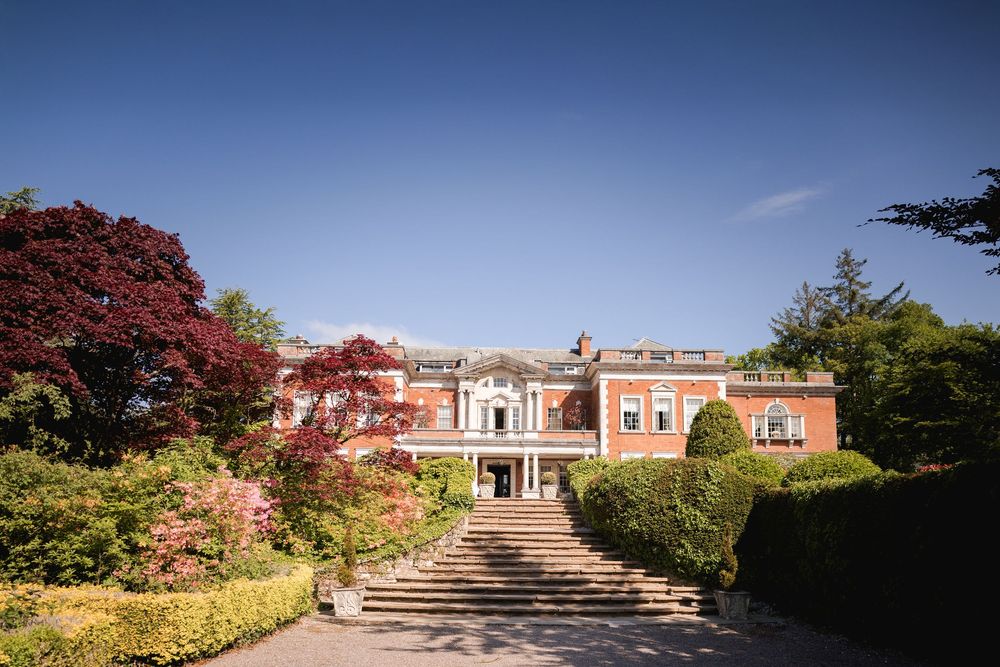 Panoramic view of a historic red brick estate with manicured grounds under blue sky.