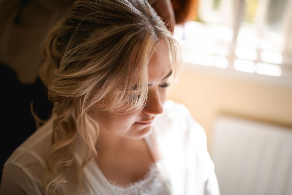 Soft natural light illuminates a bridal preparation scene through window.