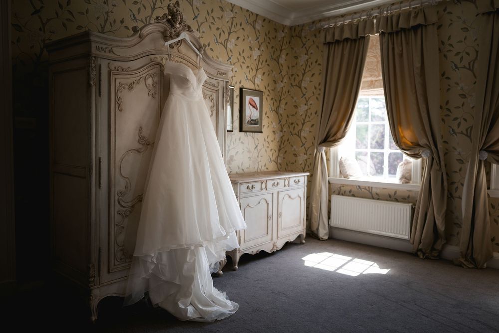 Elegant bridal preparation room with ornate wallpaper and sunlight streaming through vintage windows.