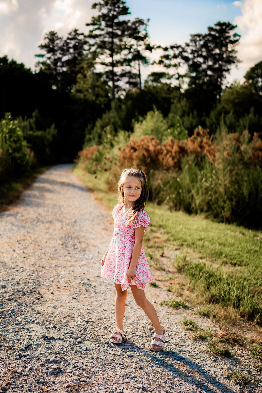 Young child in pink dress skipping along a gravel country path on a sunny summer afternoon.