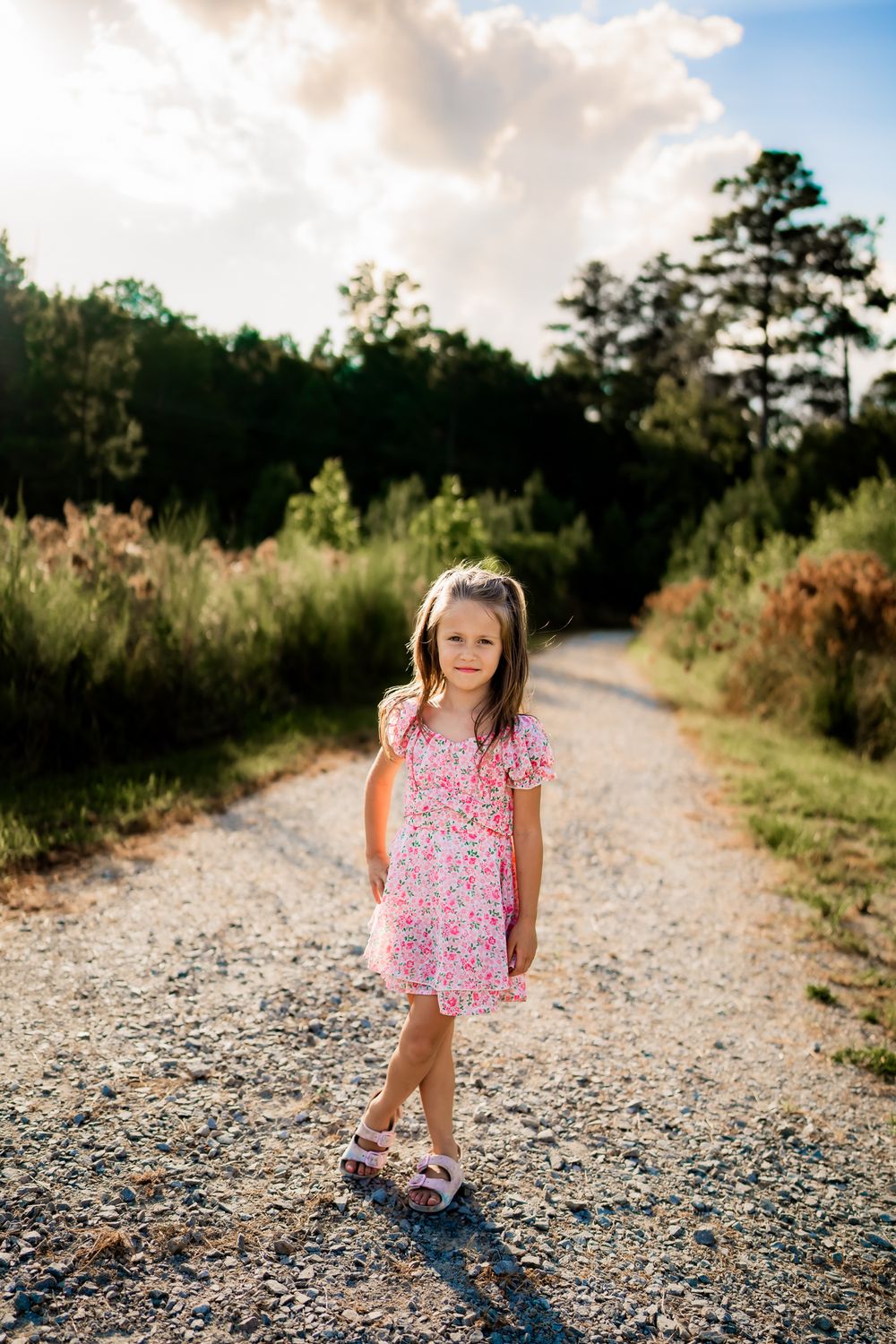 A series of lifestyle photos showing a child in a pink floral dress walking and playing on a sunlit gravel path in nature.