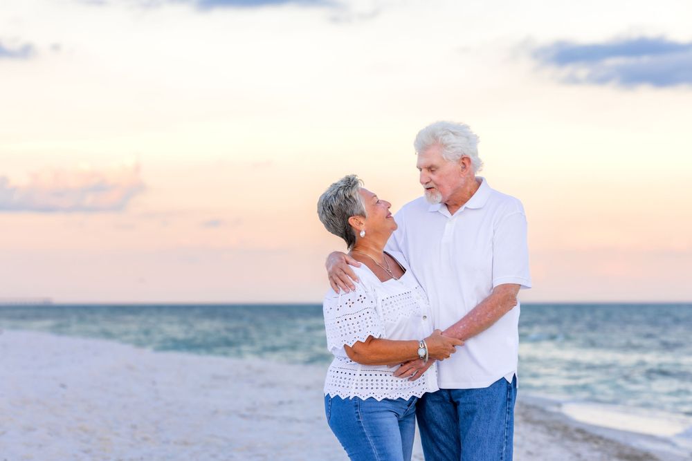 A loving couple embraces while enjoying a sunset walk along a peaceful beach with ocean waves in the background.
