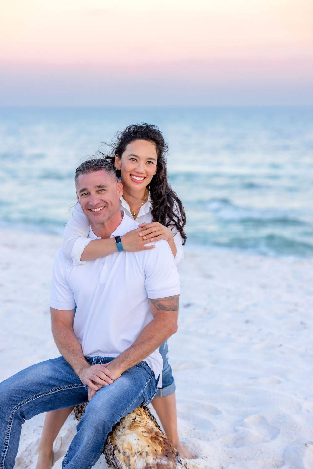 Couple sharing tender moments on white sandy beach at sunset with ocean waves in background.