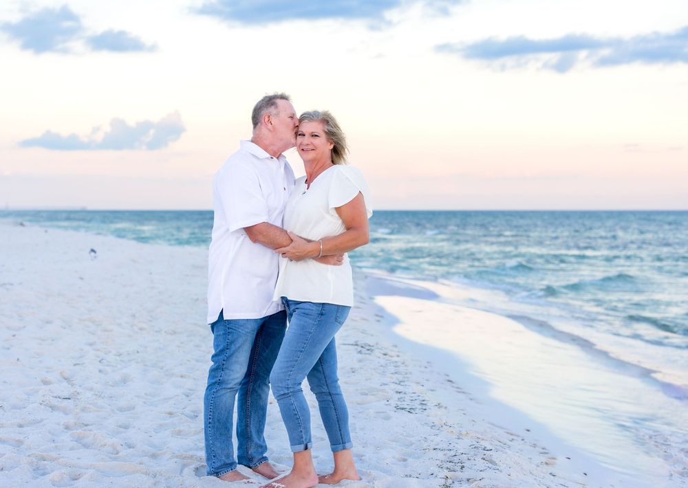 A couple walking together along the beach in white and denim blue outfits at sunset.