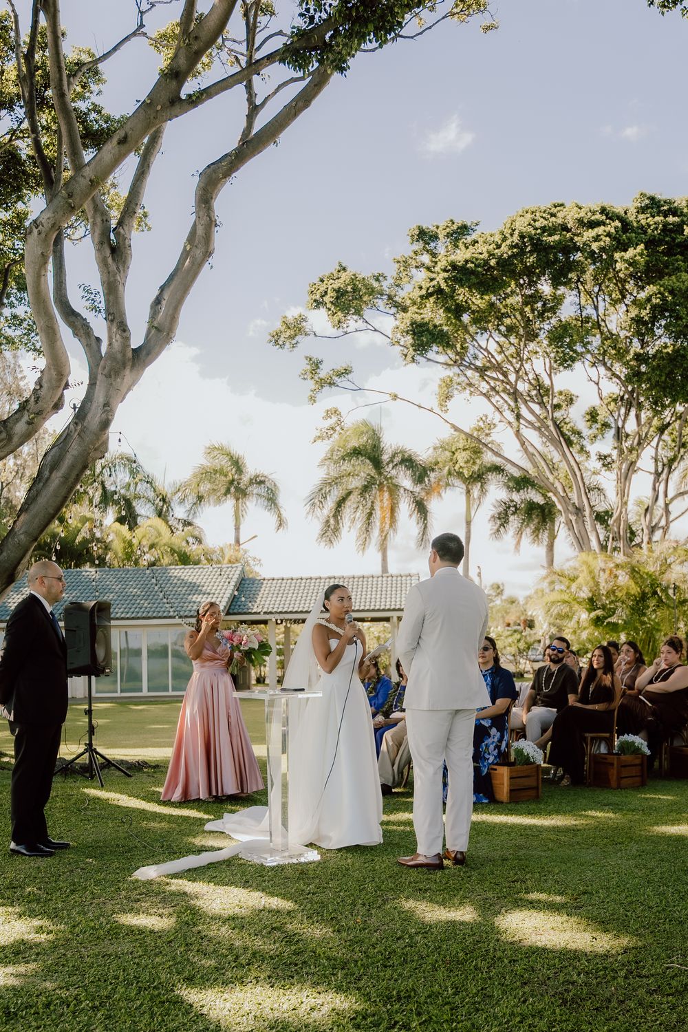 An outdoor wedding ceremony under palm trees with guests seated on a manicured lawn.