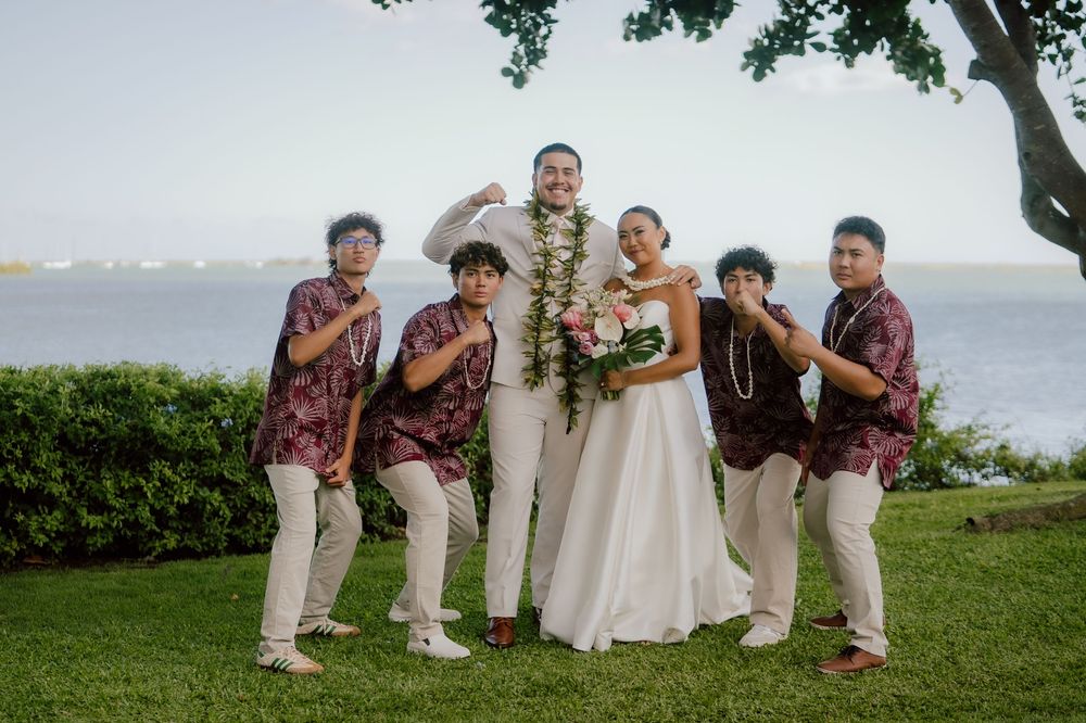 Wedding party poses together outdoors on grassy lawn with ocean and trees in background.