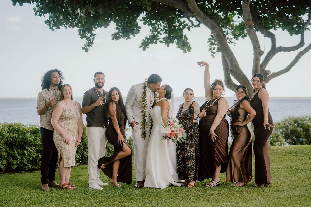 Wedding party group photo taken outdoors with ocean view in the background.