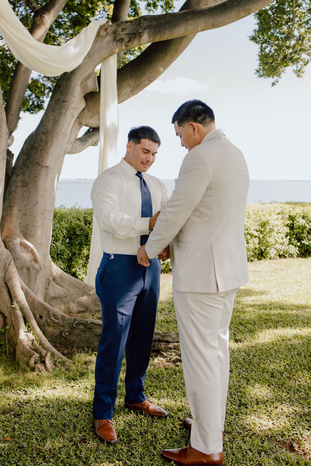 Wedding ceremony participants in white and navy attire standing beneath a large tree.