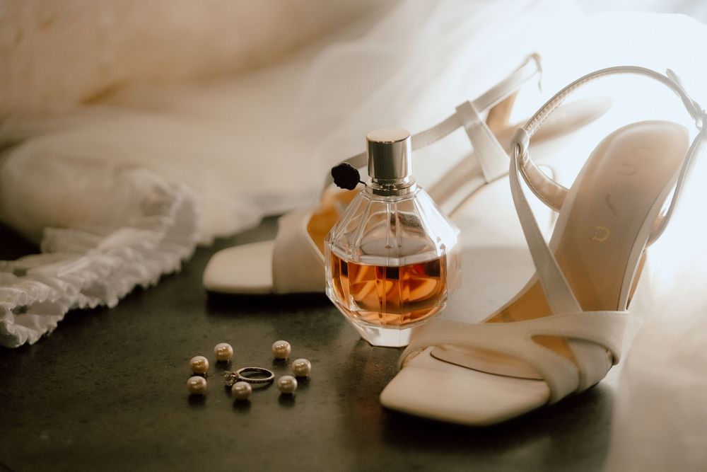 White wedding shoes, rings, and perfume arranged artistically in soft natural lighting.
