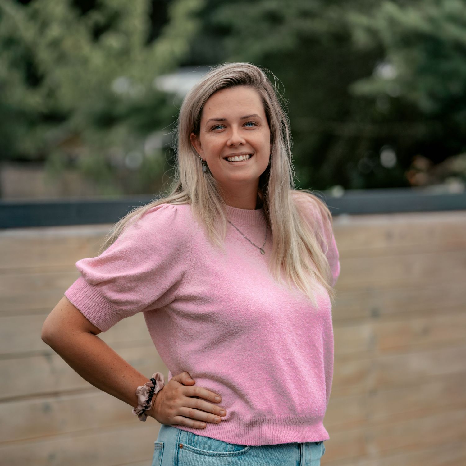 Casual outdoor portrait of someone wearing a pink shirt and light blue pants.