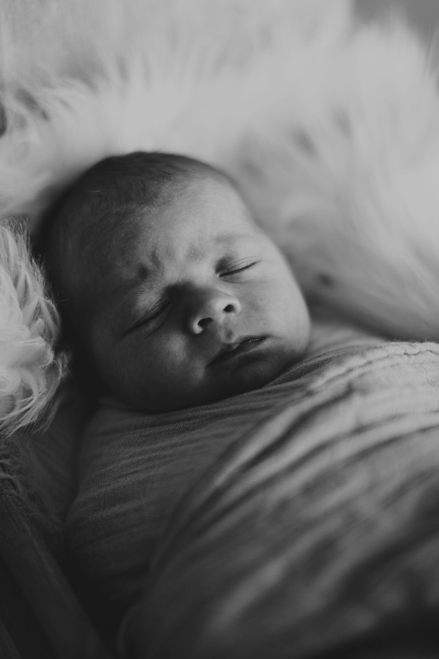 Close-up black and white portrait of a sleeping newborn baby on soft white bedding.