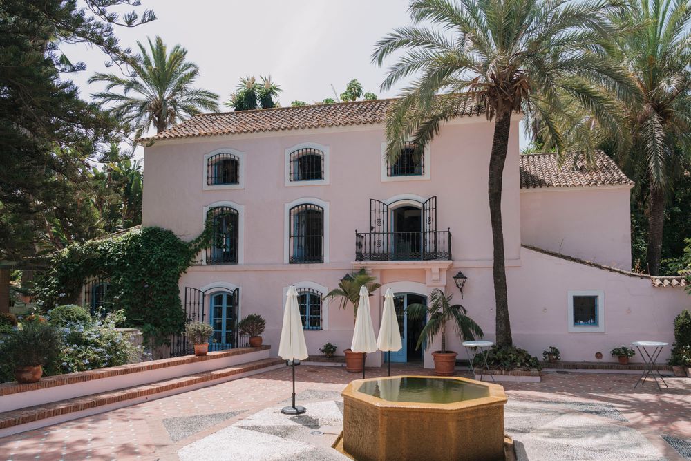 Pink Mediterranean-style villa with white trim and central fountain in courtyard.