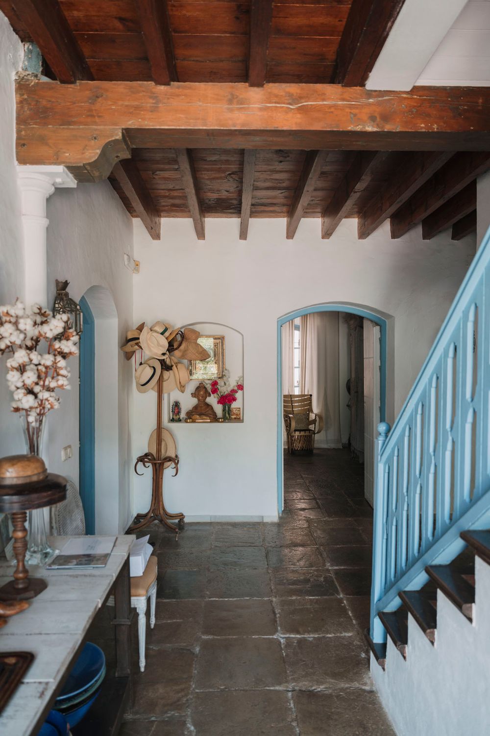 Rustic interior hallway with exposed wooden beams and blue staircase railing.