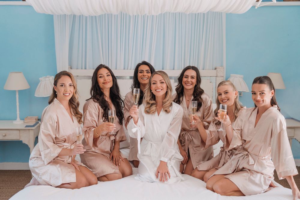 Bridal party wearing matching robes sitting together on a bed with blue wall backdrop.