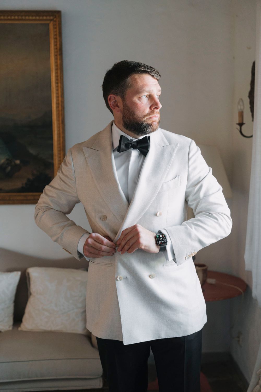 Person wearing white double-breasted dinner jacket poses against neutral wall with artwork.