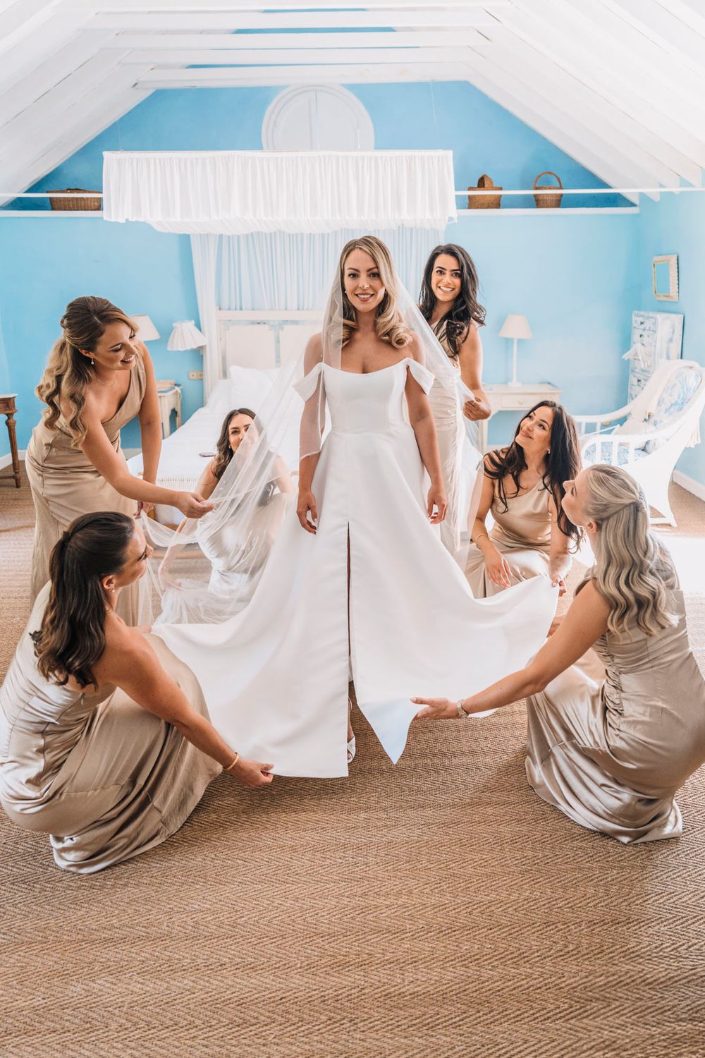 Wedding party arranges bride's dress during pre-ceremony preparations in blue and white room.