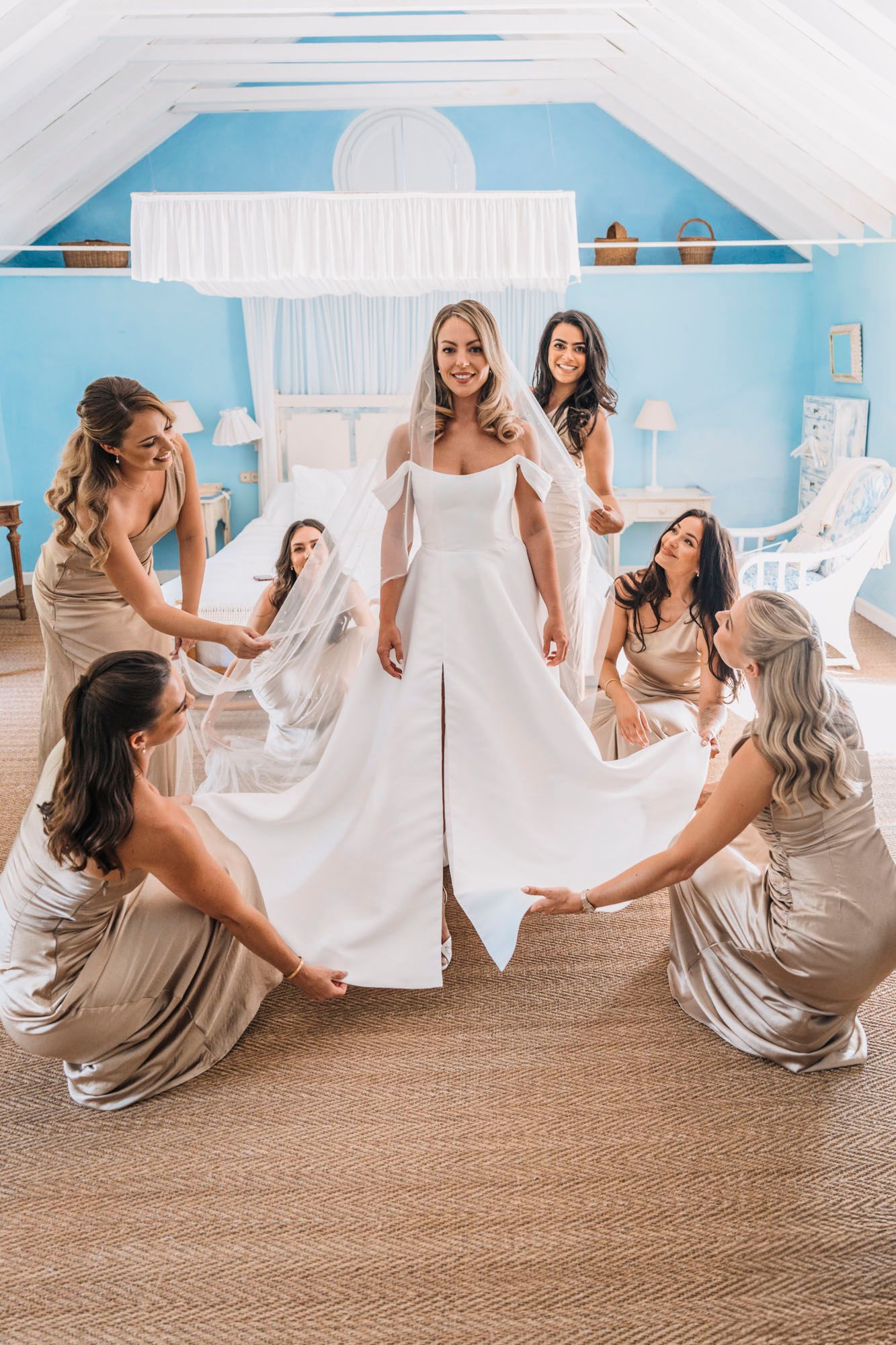 Wedding party arranges bride's dress during pre-ceremony preparations in blue and white room.