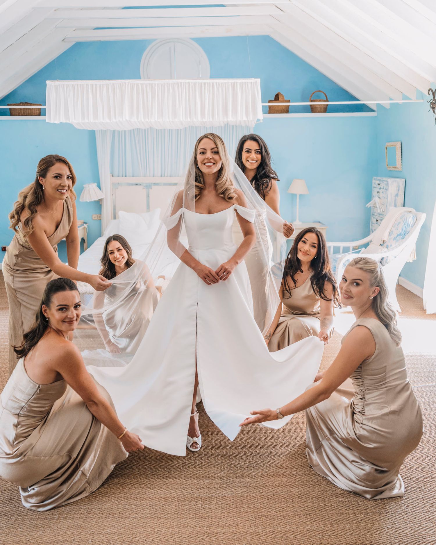 Bridal party celebrates in matching champagne dresses around bride in elegant white gown.