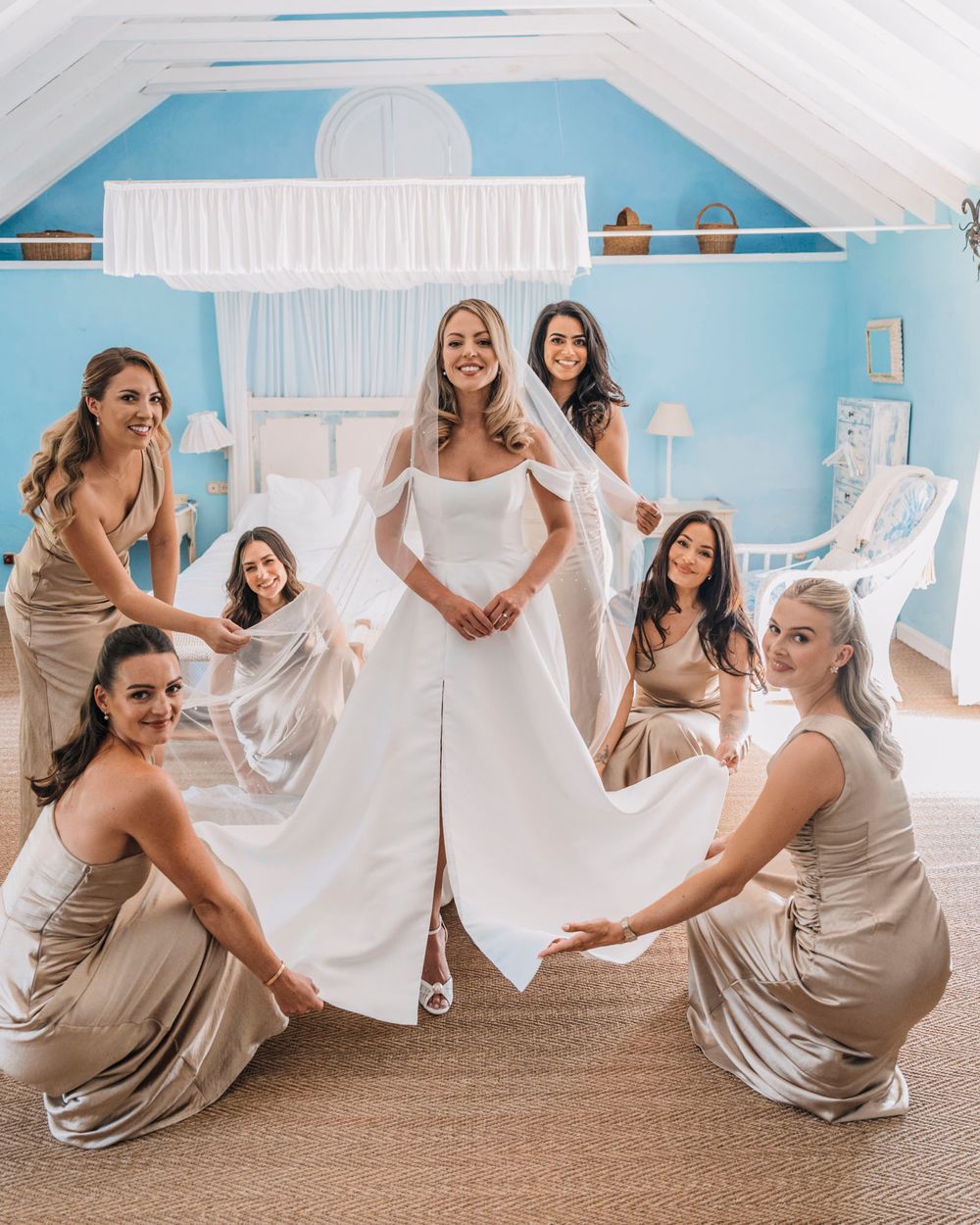 Bridal party celebrates in matching champagne dresses around bride in elegant white gown.