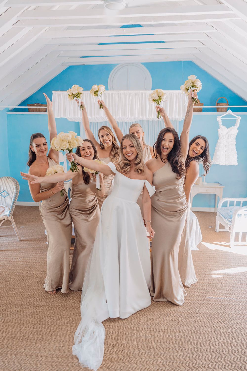Wedding party poses joyfully with bouquets in blue and white decorated room.