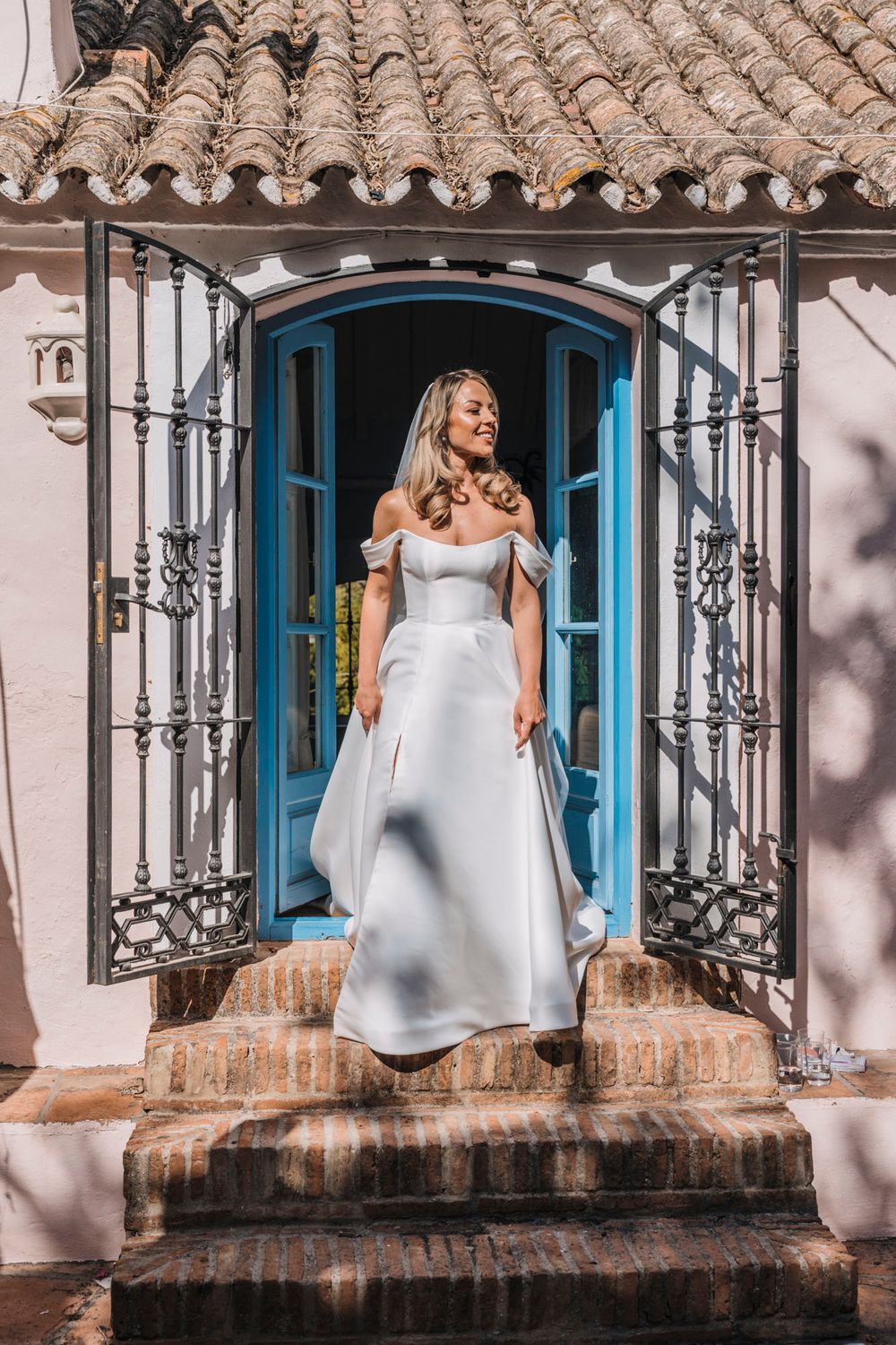 Elegant bride poses in doorway with ornate iron details and blue door frame.