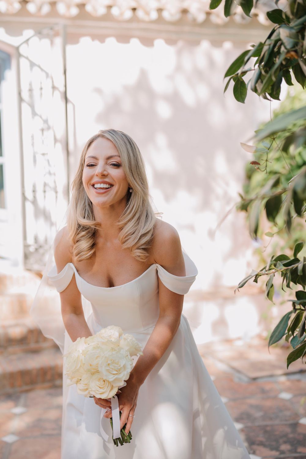 Close-up shot of a bride in a classic white off-shoulder dress holding a white floral bouquet.