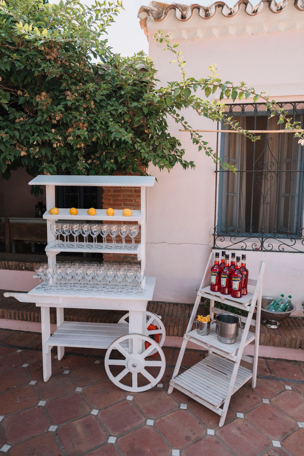Vintage-style white drink cart and ladder shelf set up for outdoor wedding reception.