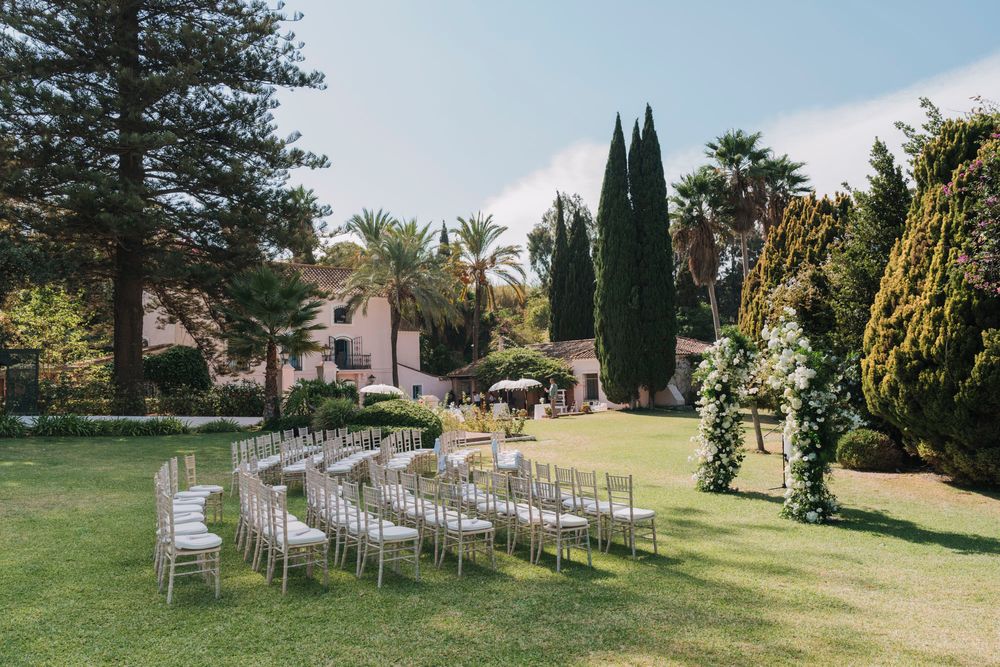 White chairs arranged in rows on a manicured lawn for an outdoor wedding ceremony.