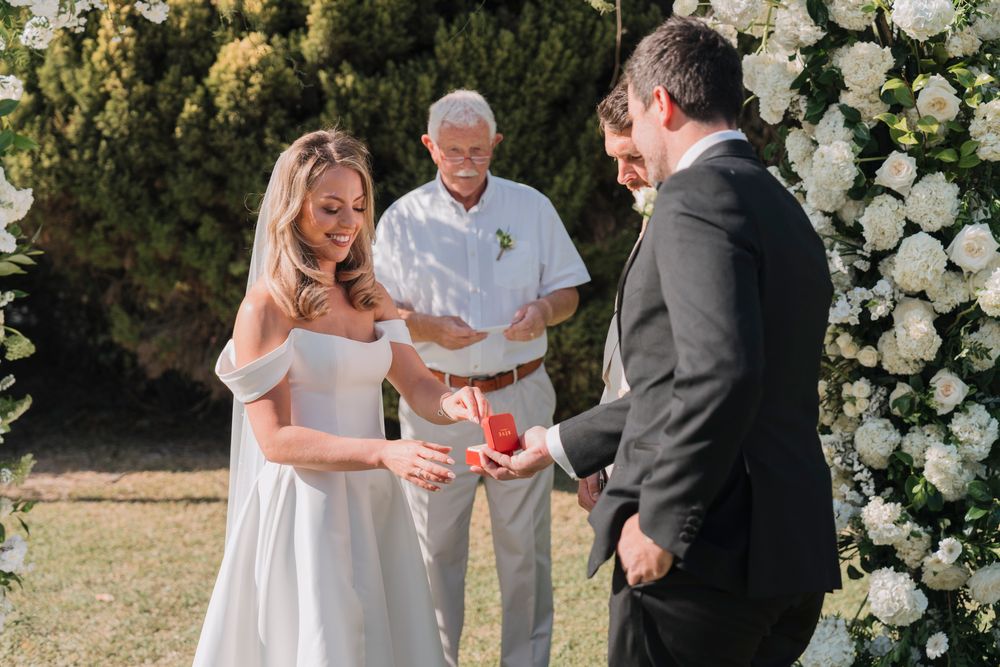 An intimate wedding ceremony moment under a lush white floral arch in a garden setting.