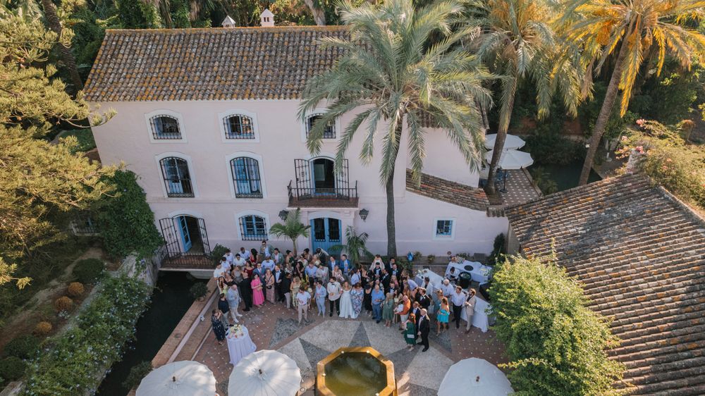 Aerial view of wedding guests gathered outside a white Spanish villa with palm trees.