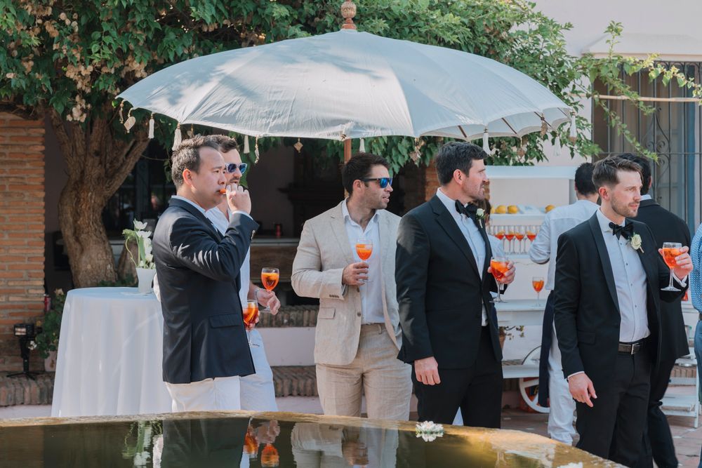 Groomsmen standing under white umbrellas at an outdoor cocktail reception.