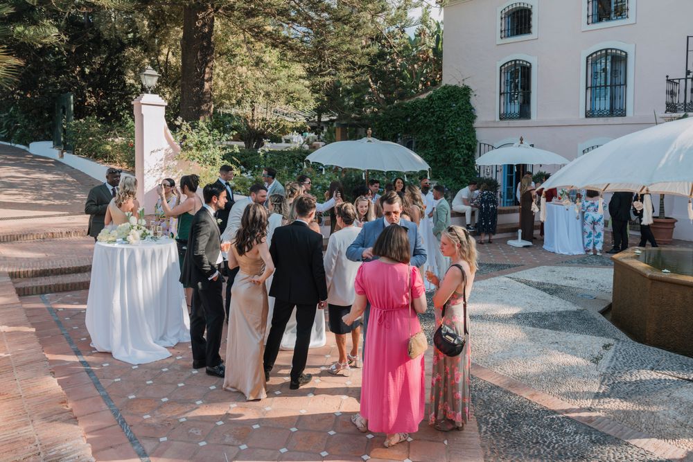 Wedding guests socializing under umbrellas at an outdoor cocktail hour.