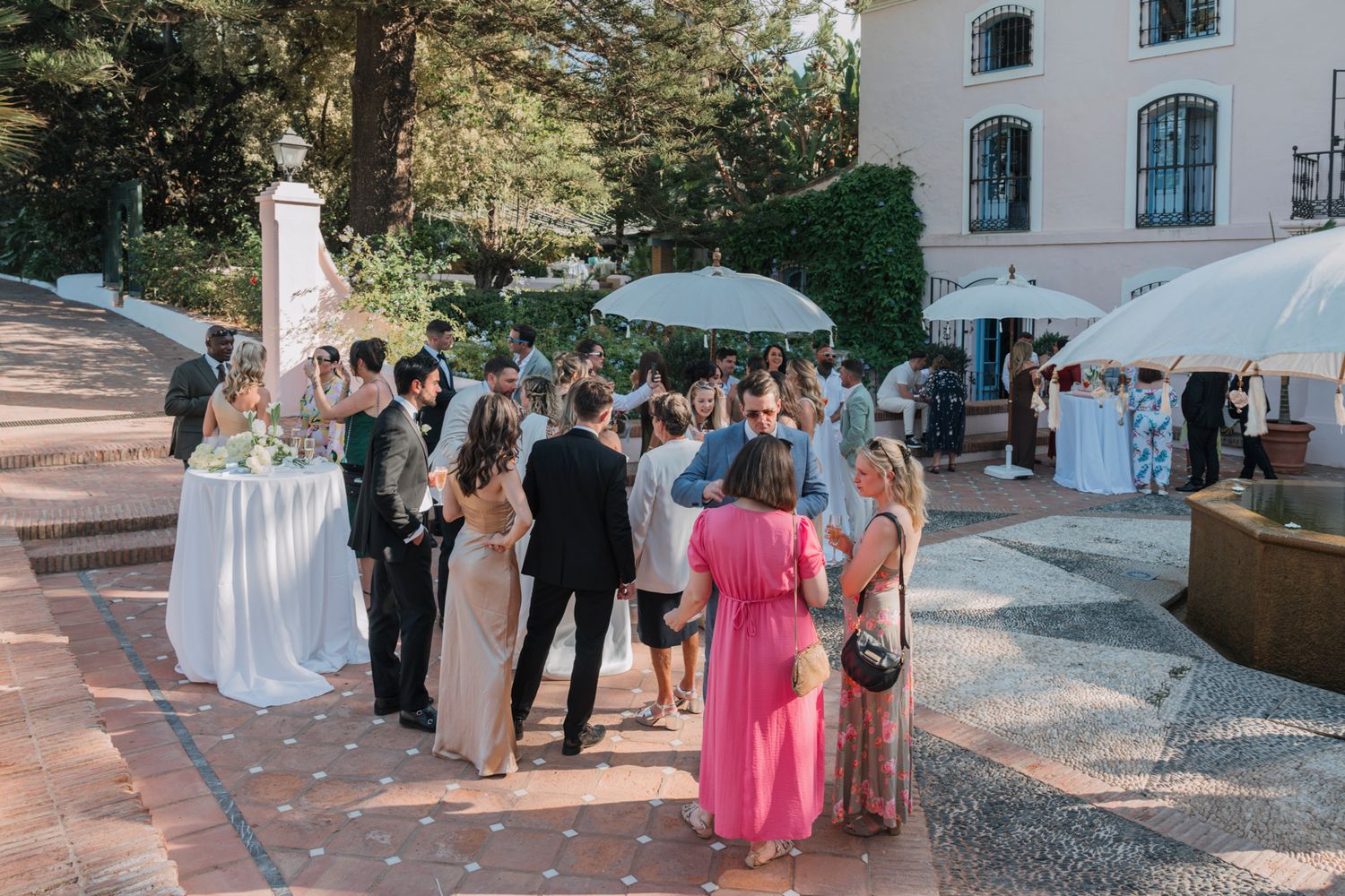 Wedding guests socializing under umbrellas at an outdoor cocktail hour.