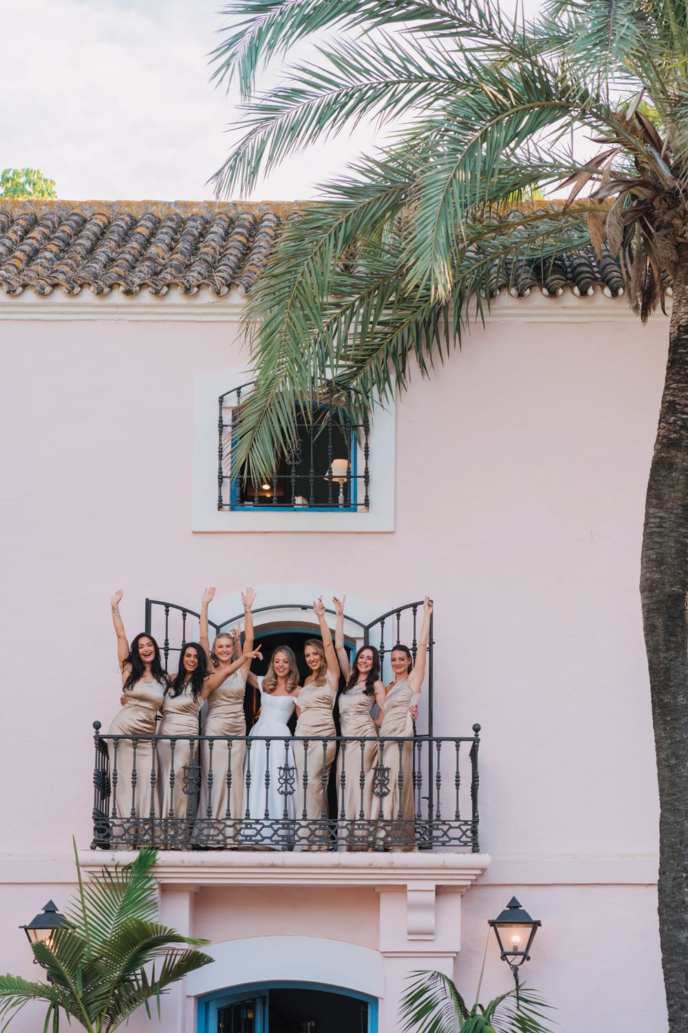 Mediterranean style villa with palm trees and wedding party on balcony celebrating.