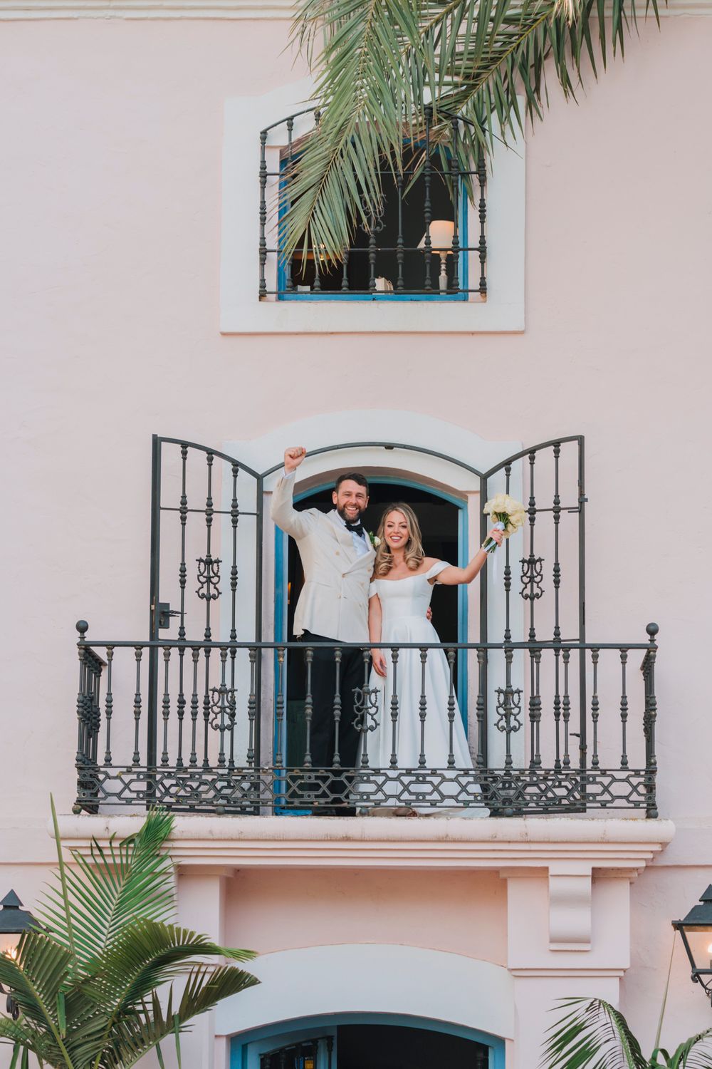 Newly married couple celebrating on a Spanish-style balcony with decorative ironwork.