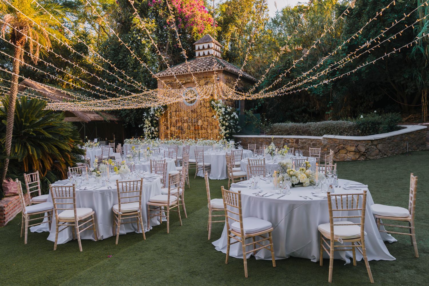 Elegant outdoor wedding reception setup with string lights and white table settings.