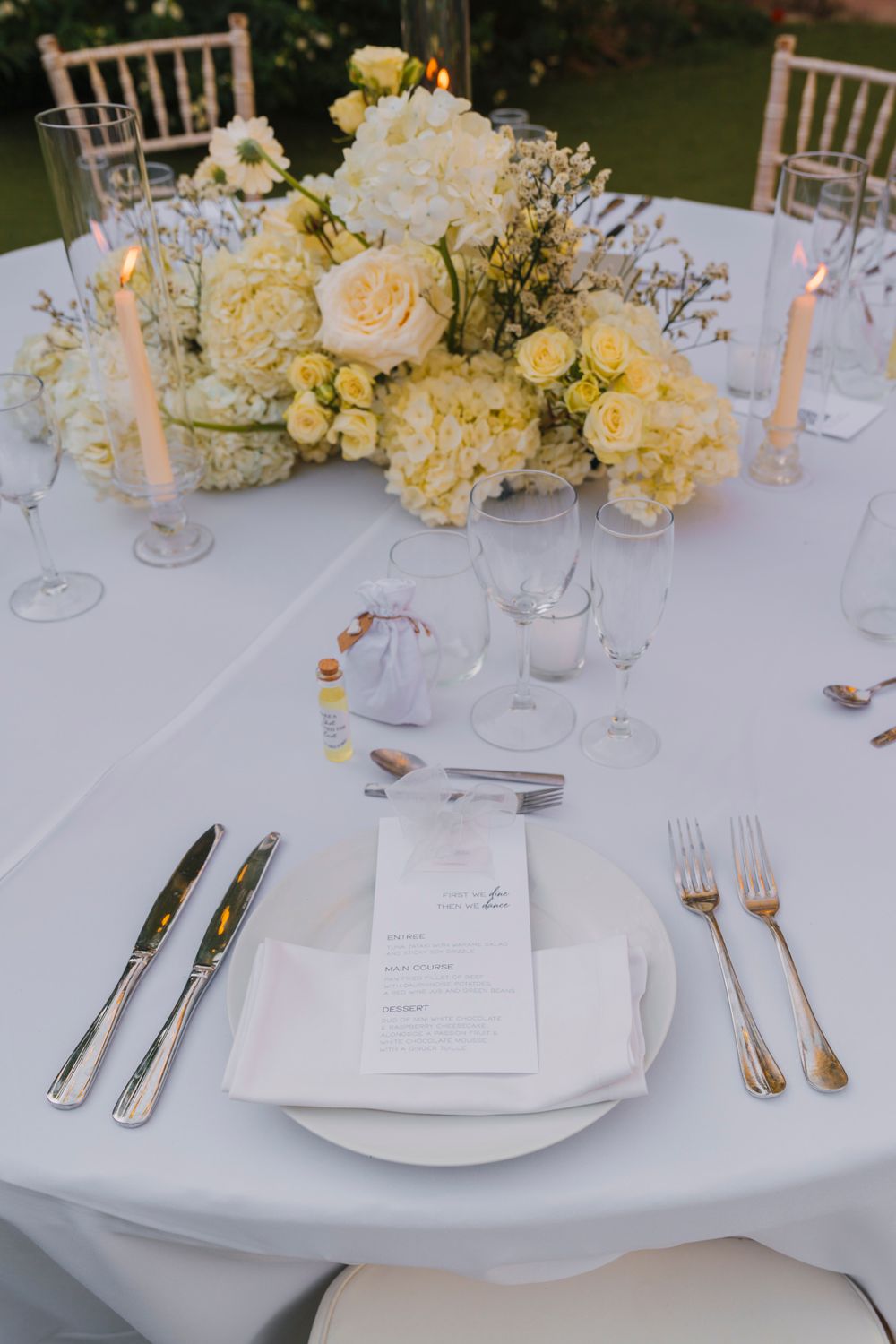 Elegant place setting with white menu card, silver cutlery, and cream floral centerpiece.