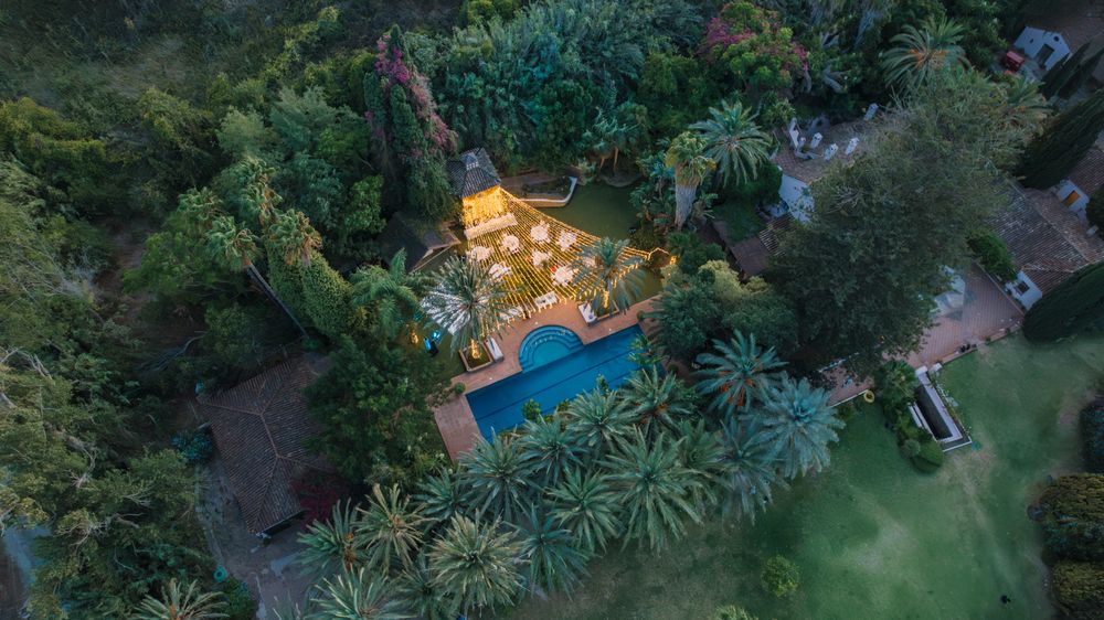 Aerial view of an illuminated luxury villa with swimming pool surrounded by lush tropical gardens at dusk.