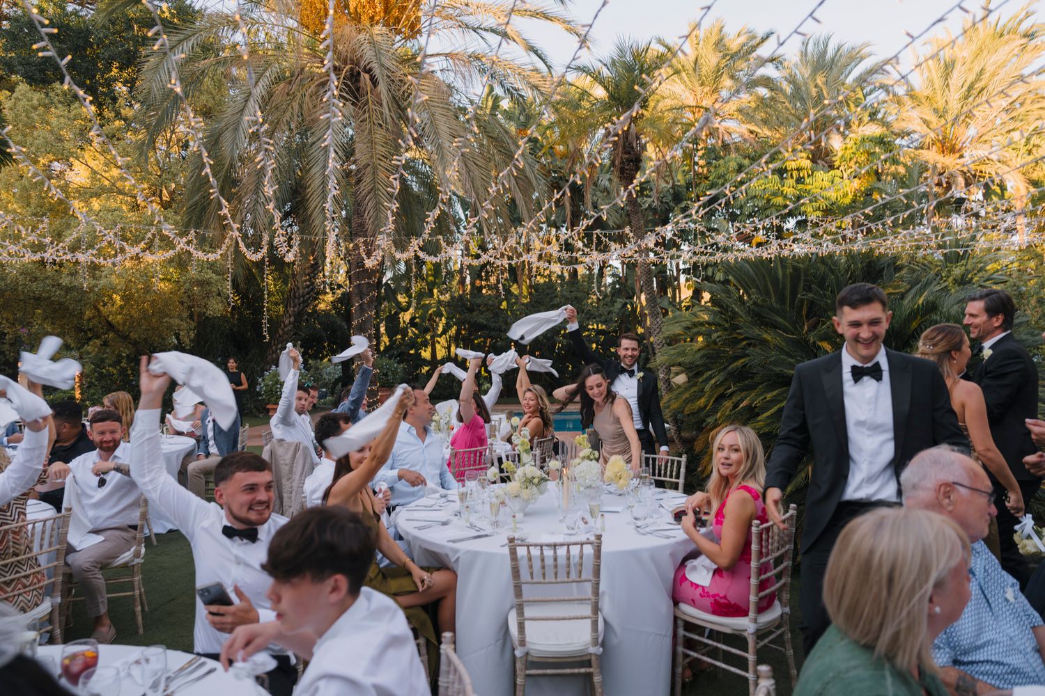 An elegant outdoor wedding reception under twinkling lights and palm trees.