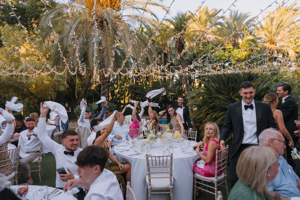 An elegant outdoor wedding reception under twinkling lights and palm trees.