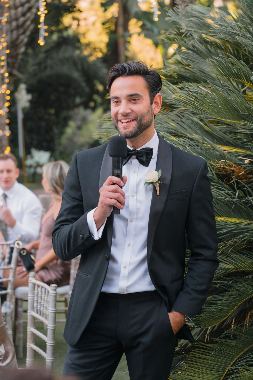 An elegant wedding speech moment at an outdoor tropical venue with palm trees.
