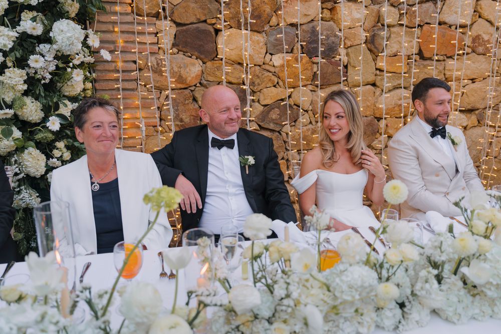 A formal wedding reception table decorated with luxurious white floral arrangements.