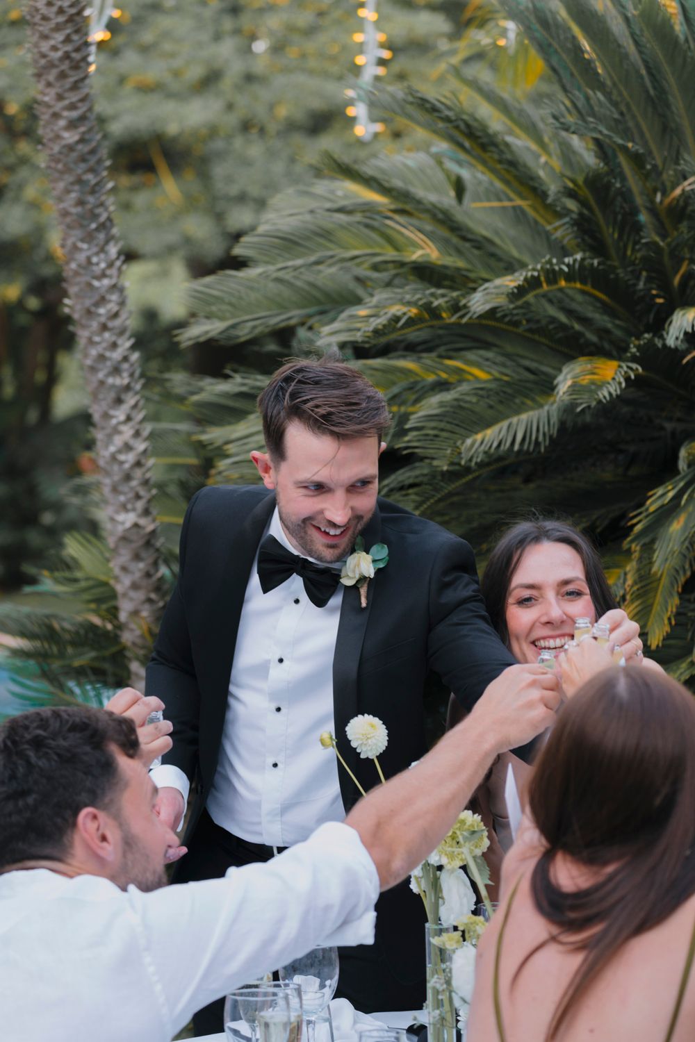 A candid moment of laughter during an outdoor wedding reception under palm trees.