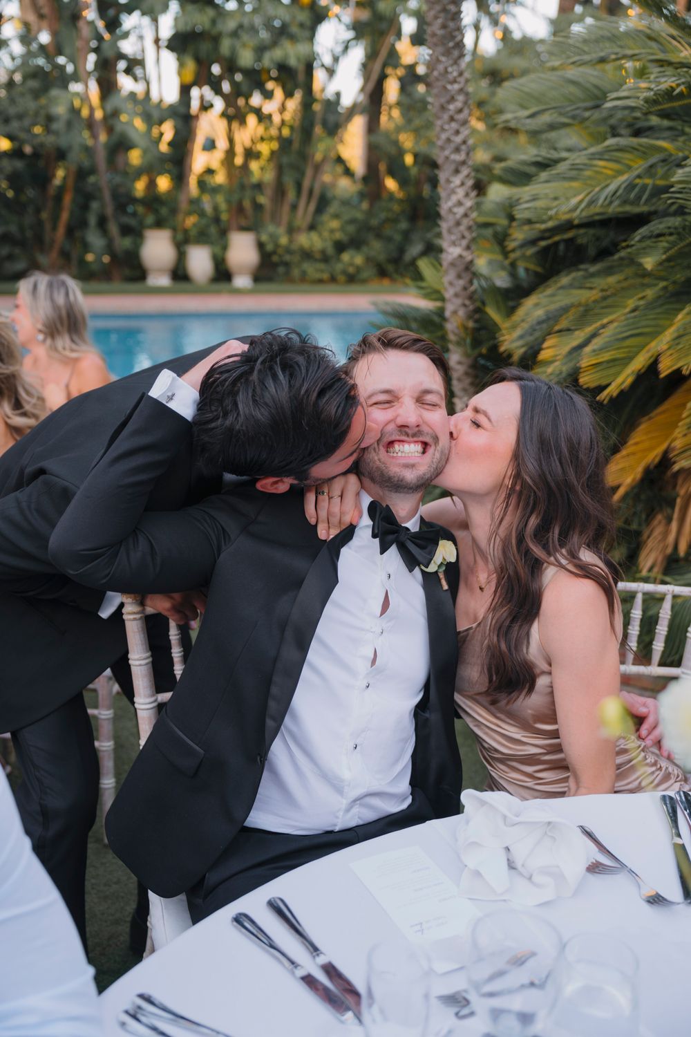 A candid moment of joy and laughter shared at an outdoor wedding reception by a pool at sunset.