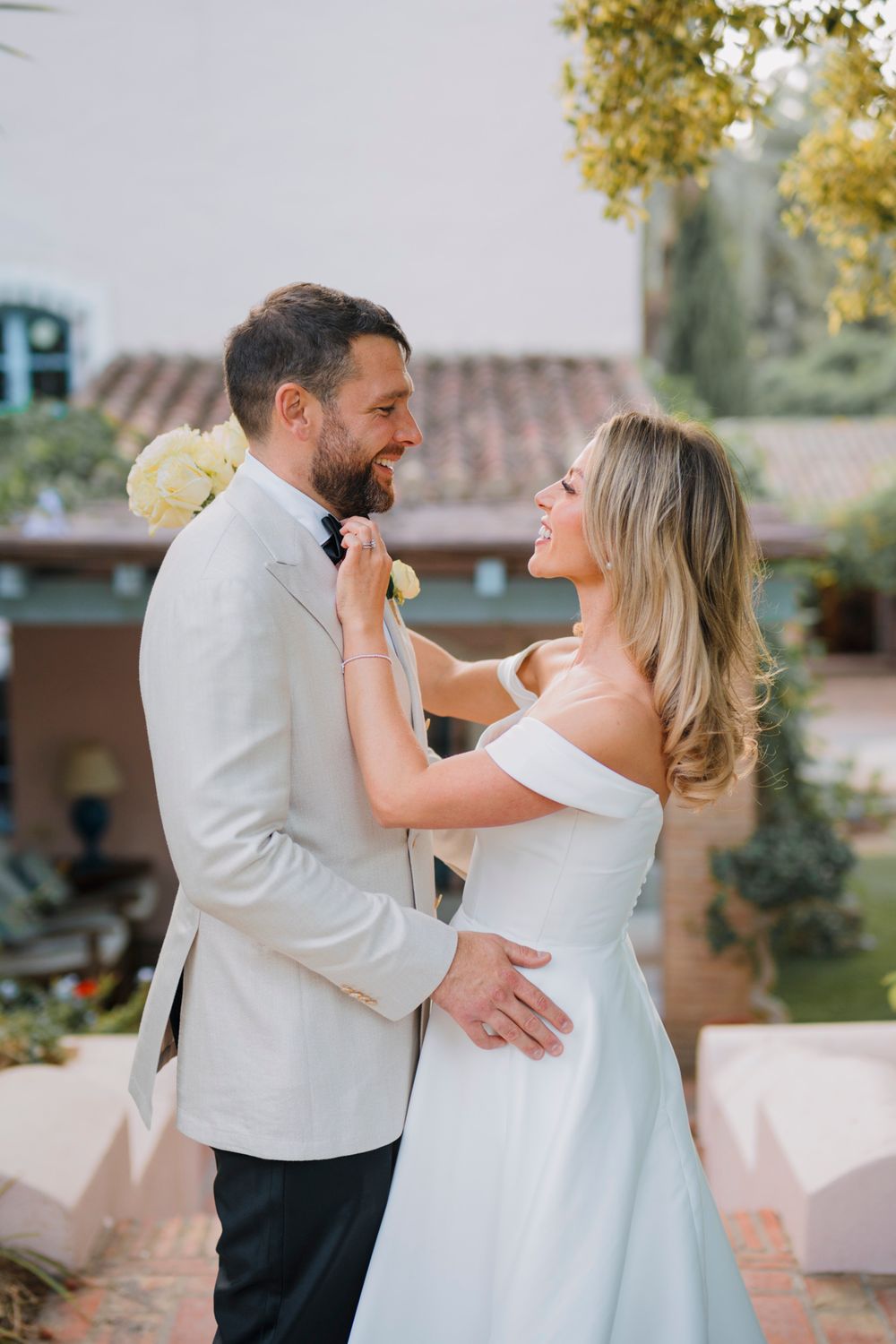 A tender moment between newlyweds posing in front of Spanish architecture and palm trees.