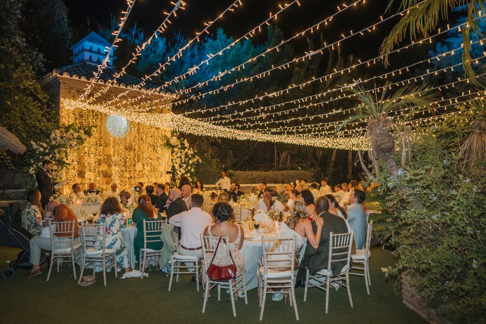 Evening wedding reception with string lights creating a magical canopy over white chairs and tables.