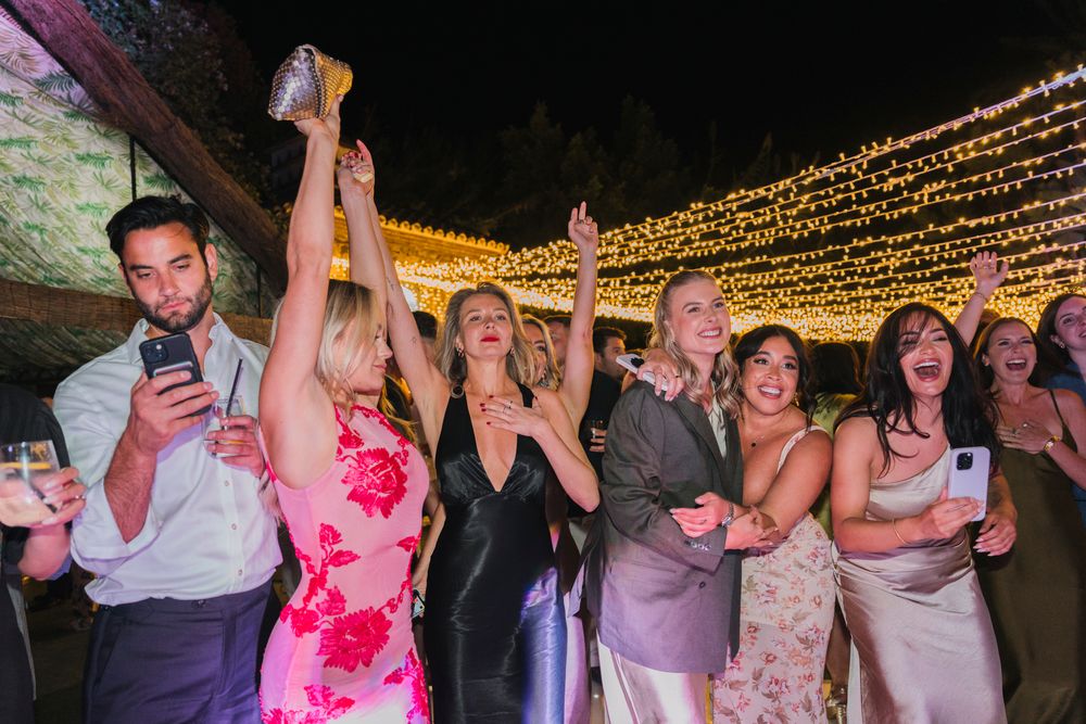 Wedding guests celebrate joyfully under twinkling string lights at an outdoor evening reception.