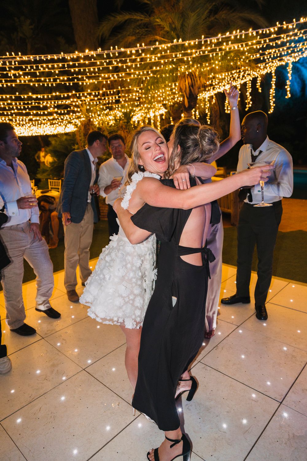 A celebratory dance moment on an outdoor patio illuminated by overhead string lights.