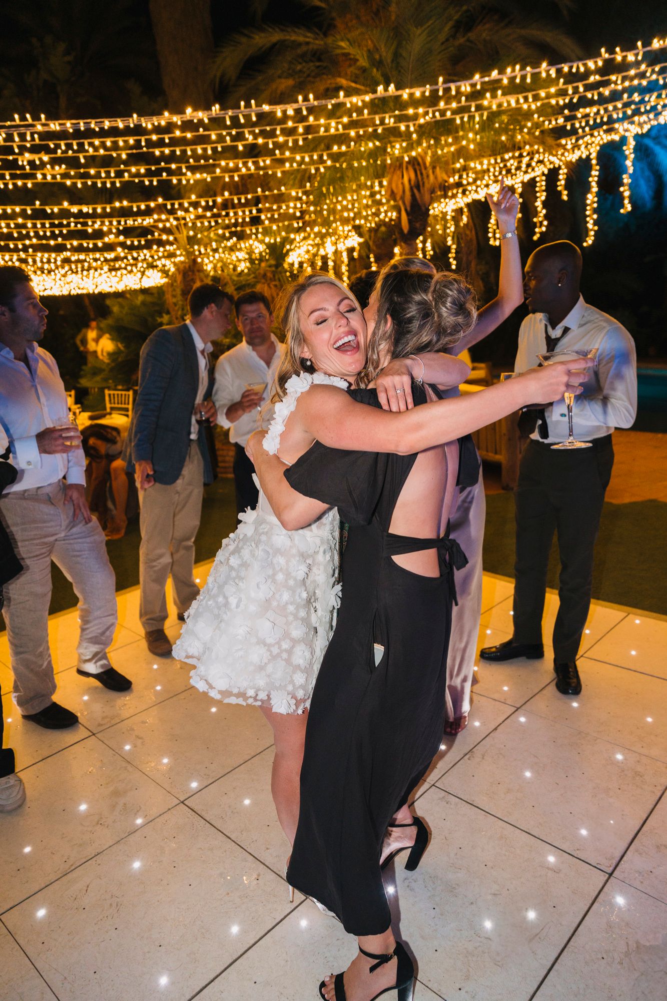 A celebratory dance moment on an outdoor patio illuminated by overhead string lights.