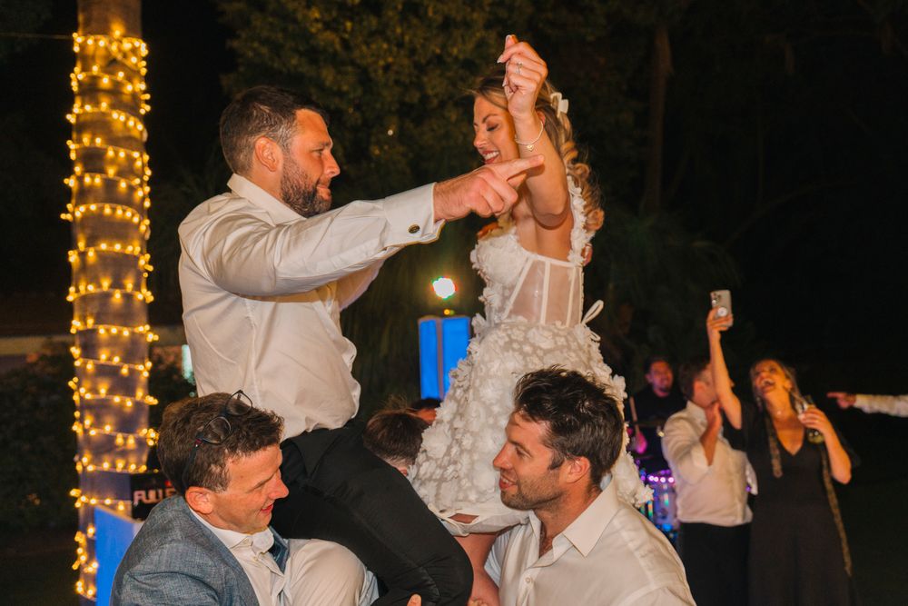 Celebration peaks during a festive dance moment under twinkling lights at an outdoor reception.